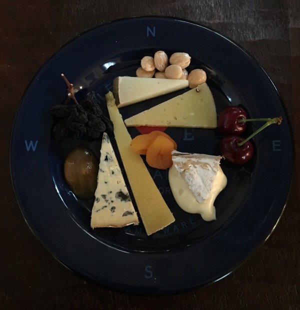 Plate with five different cheeses and a variety of fruits and nuts
